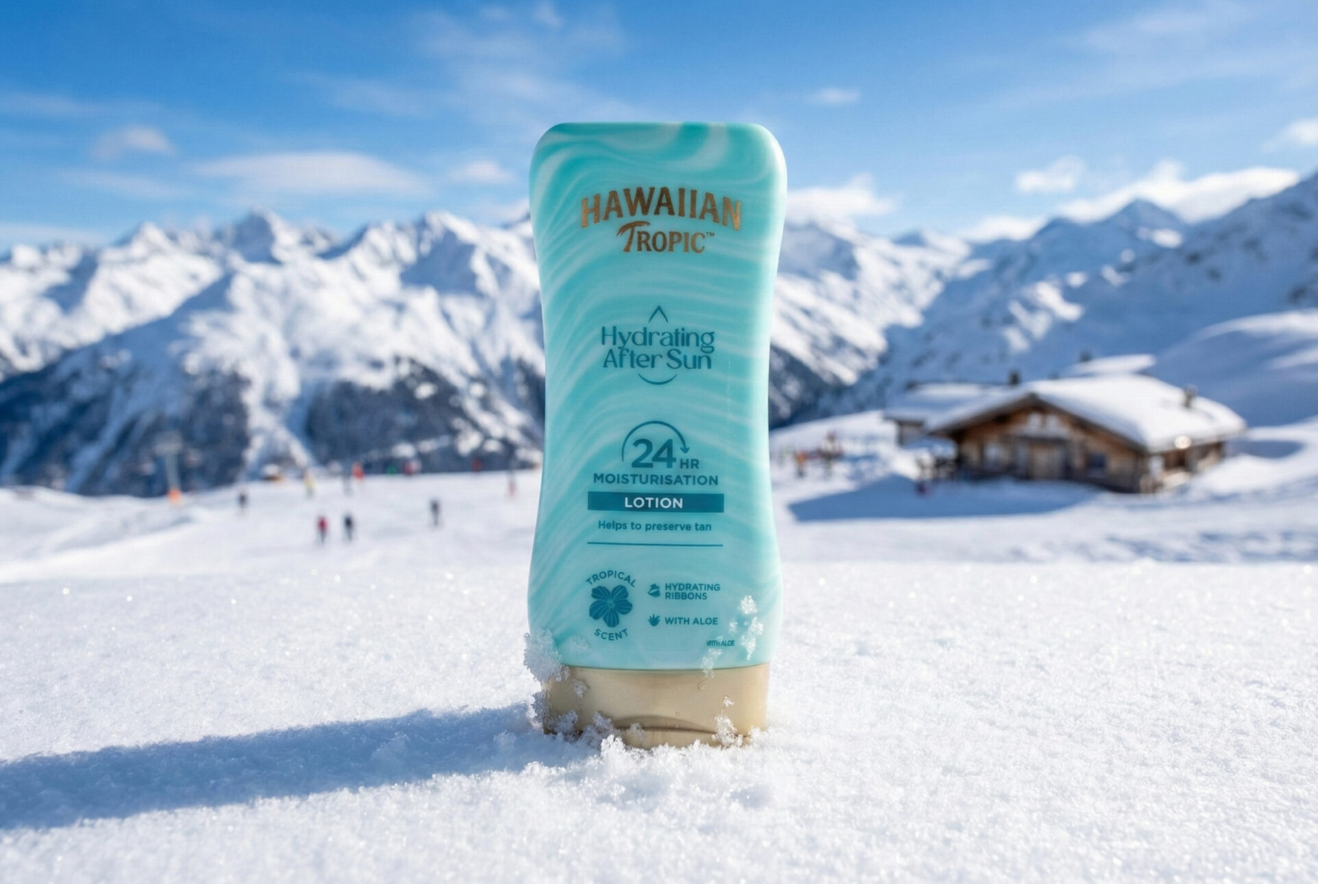 Eine türkisfarbene After Sun Lotion steht im Schnee. Im Hintergrund sind Schneebedeckte Berge und eine Skihütte zu sehen.