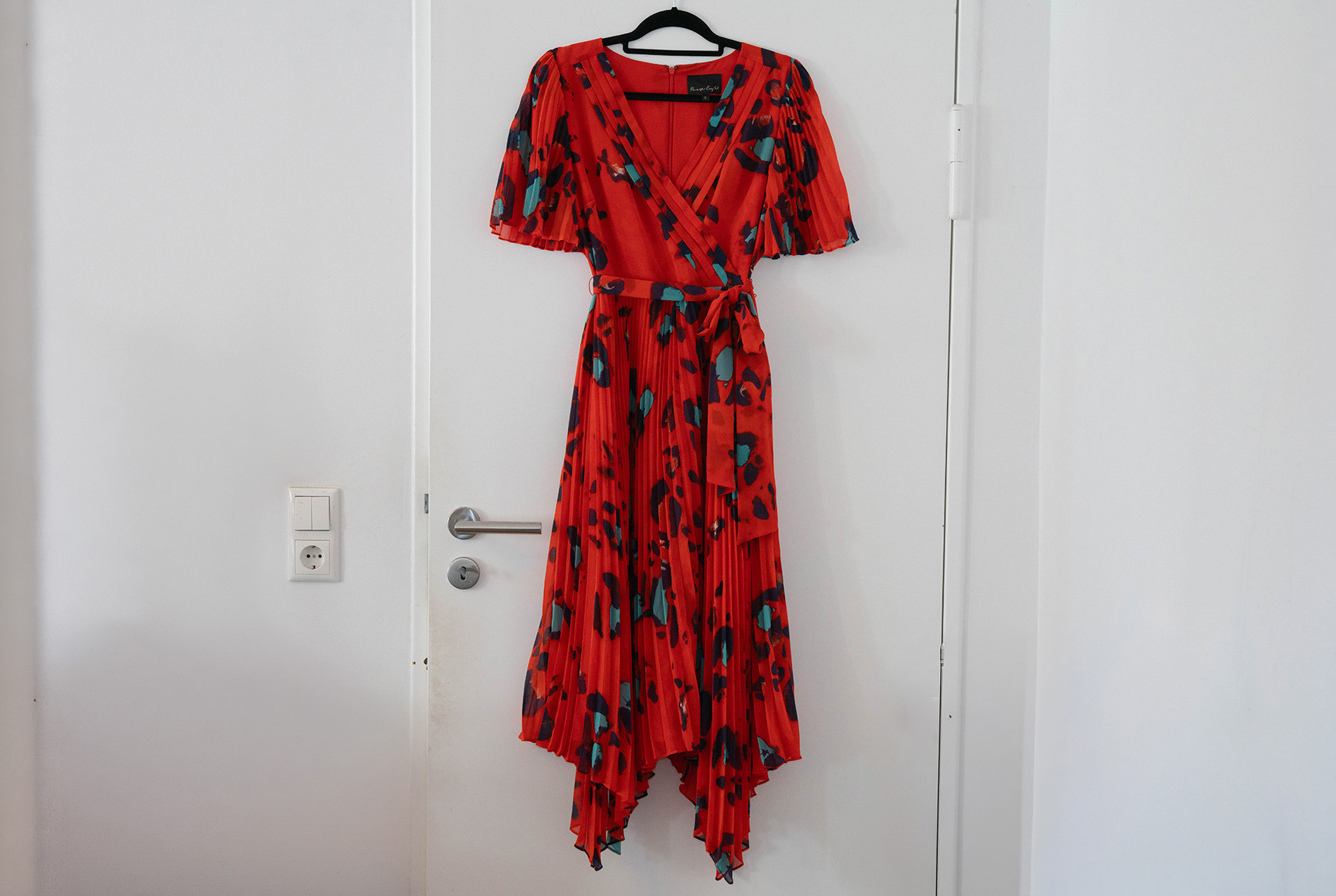 Ein rotes kleid mit Türkisem Leopardenmuster hängt auf einem Kleiderbügel an einer Zimmertür.