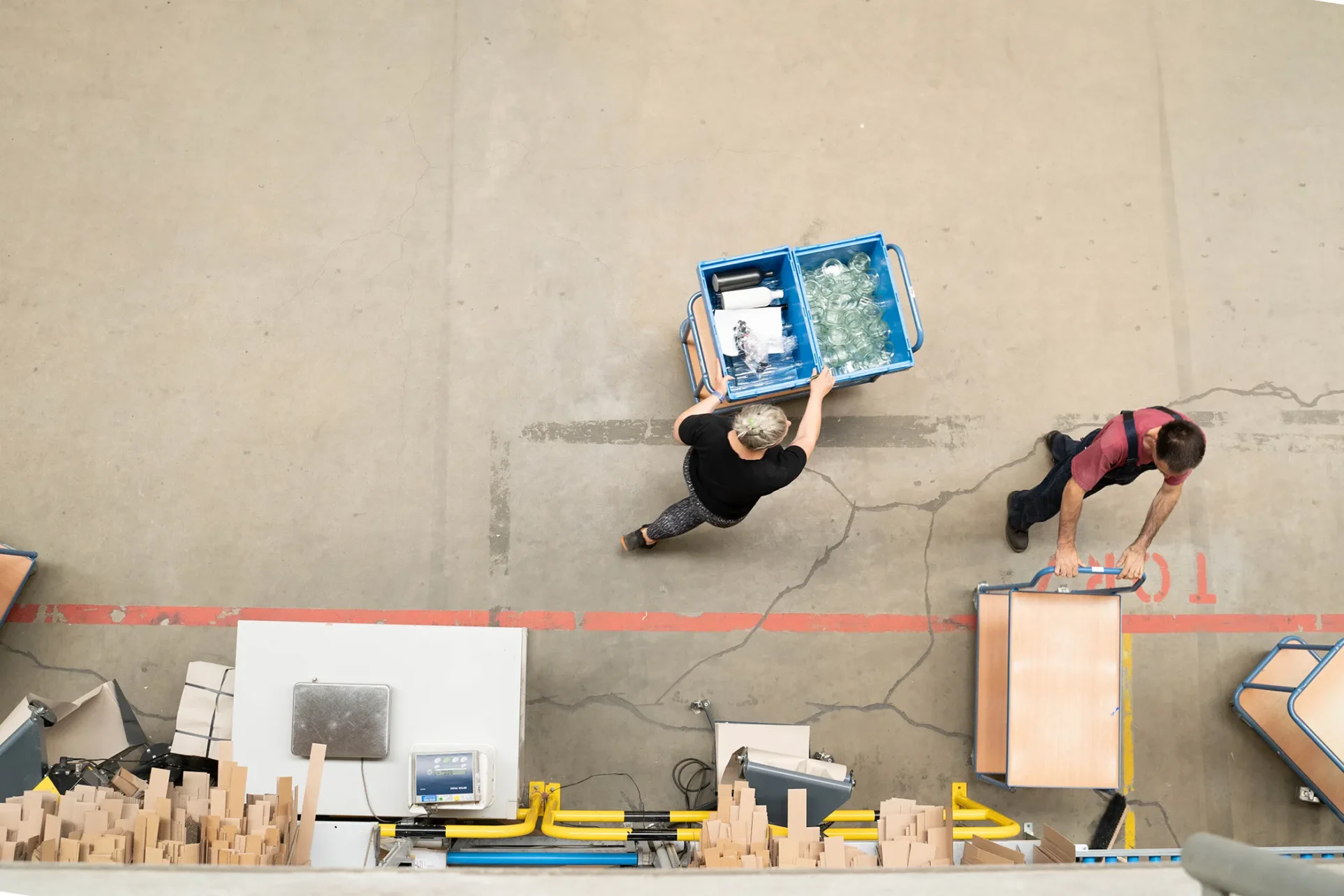 Eine Frau in einer Fabrikhalle schiebt einen Wagen mit Produkten