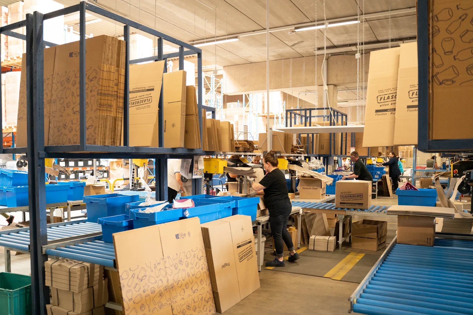 Die Verpackungsstation in einer Lagerhalle. Im Vordergrund stehen lehre Kartons.