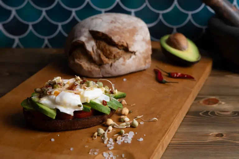 Ein Toast mit Avocado, Sprossen und Ei auf einem Holzbrett vor einem grünen Hintergrund