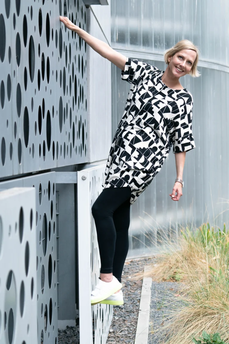 Eine junge Frau in einem schwarz-weißen Kleid hält sich an einer Kletterwand fest.