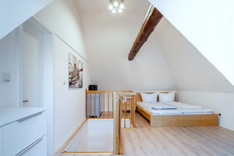 Blick in ein Schlafzimmer in einem Dachgeschoss. Hohe Decken und Dachschrägen, eine offene Treppe nach unten