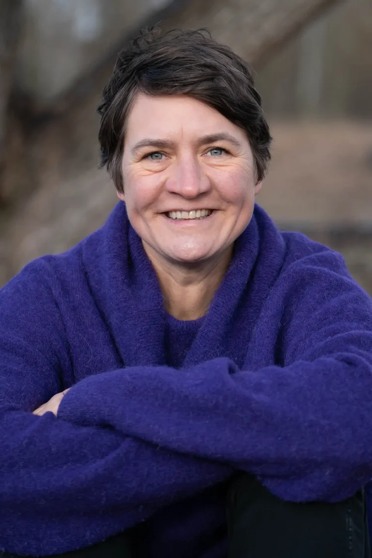 Eine Frau in einem lila Pullover lächelt in die Kamer