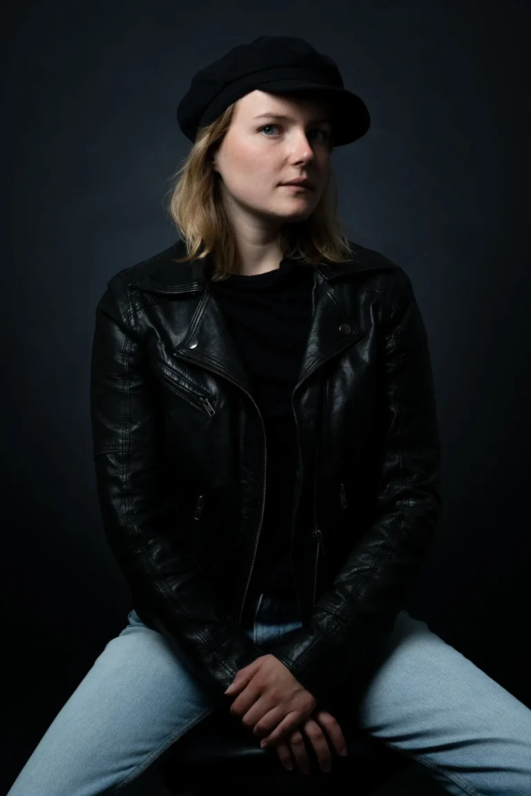 Eine junge Frau in einer schwarzen Jacke blickt seitlich in die Kamera