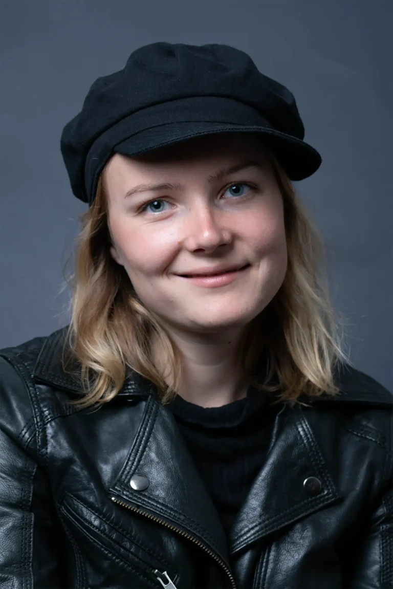 Eine junge Frau in einer schwarzen Jacke blickt seitlich in die Kamera