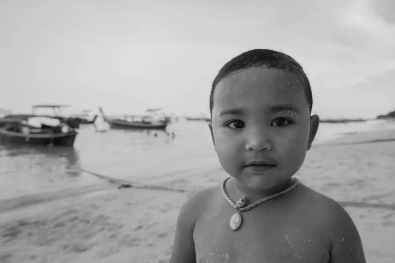 Ein kleiner Junge mit Sand im Gesicht steht an einem Strand.
