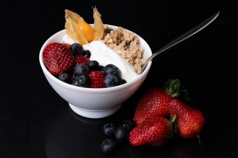 Eine Schüssel mit Beeren, Granola und Joghurt auf einem schwarzen, spiegelden Hintergrund.